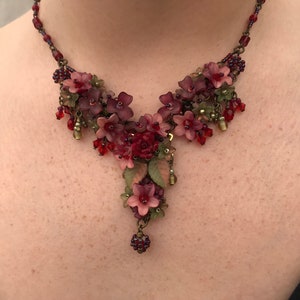 Peut inclure: Un collier floral délicat avec des fleurs et des perles roses, rouges et vertes. Le collier est en métal et a un style vintage.