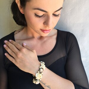 May include: A close-up of a woman's arm wearing a white and pink floral bracelet. The bracelet is made of small flowers and pearls. The woman has a tattoo on her arm that says "sola far niente".