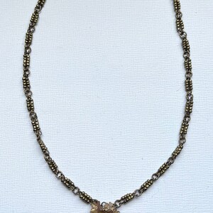 May include: Vintage-style brass necklace with a floral pendant and leaf detailing. The necklace has a delicate chain and a hook clasp. The pendant features a cluster of small beads hanging from the bottom, creating an elegant look.