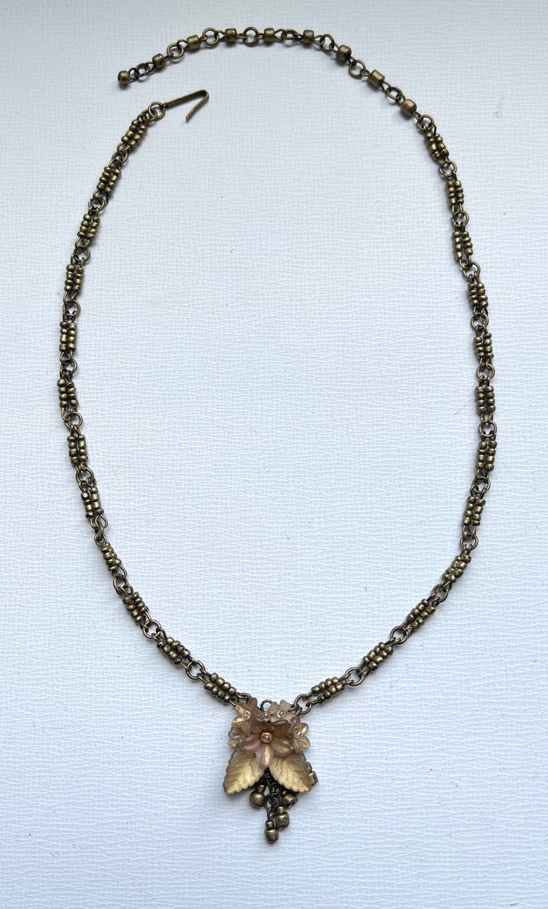 May include: Vintage-style brass necklace with a floral pendant and leaf detailing. The necklace has a delicate chain and a hook clasp. The pendant features a cluster of small beads hanging from the bottom, creating an elegant look.