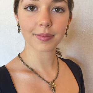 May include: A vintage jewellery set featuring a necklace and matching earrings. The necklace has a delicate chain with a floral pendant. The earrings are dangling, with a similar floral design. The jewellery is a muted gold colour.