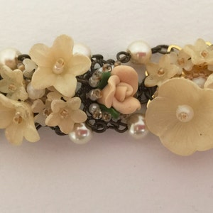 May include: A delicate floral bracelet featuring a chain with faux pearls and pastel pink and cream flowers.
