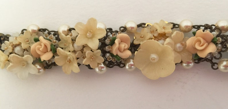 May include: A delicate floral bracelet featuring a chain with faux pearls and pastel pink and cream flowers.