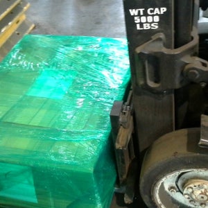 May include: A green pallet wrapped in plastic shrink wrap is being loaded onto a forklift. The forklift has a weight capacity of 5000 lbs.