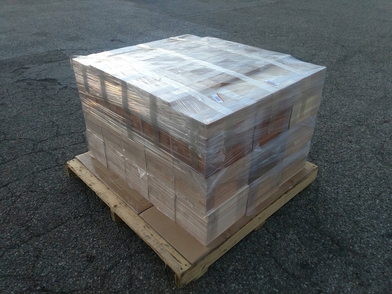 May include: A stack of wooden boxes wrapped in clear plastic, sitting on a wooden pallet. The boxes are stacked in a rectangular shape and are all the same size.
