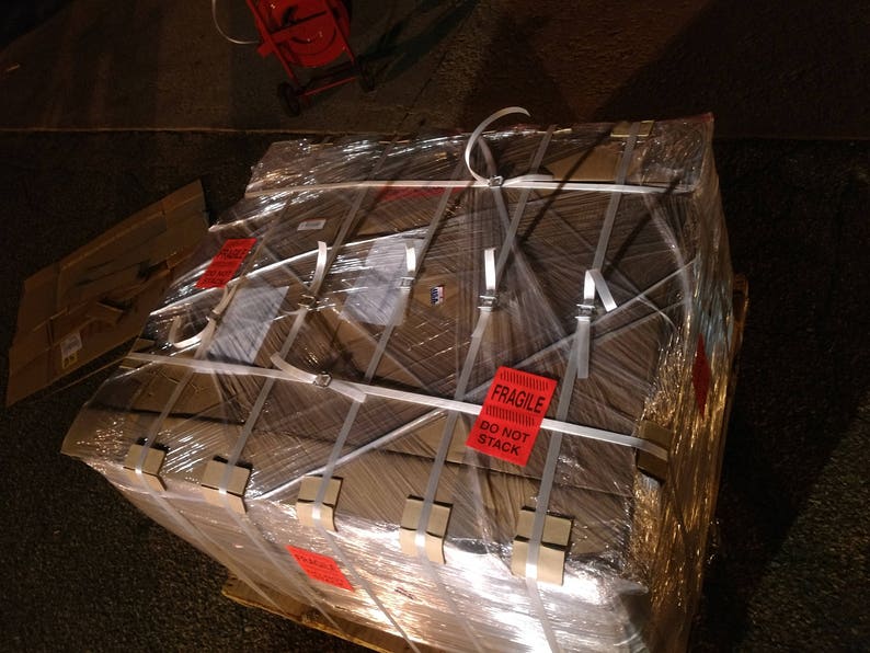 May include: A large cardboard box wrapped in clear plastic and secured with white straps. The box is labeled "Fragile, Do Not Stack".