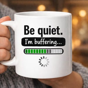 Puede incluir: Taza de cerámica blanca con el texto "Be quiet. I'm buffering..." en negro. La taza presenta un gráfico de barra de carga y un icono de carga. La taza tiene un asa y está diseñada para bebidas calientes.