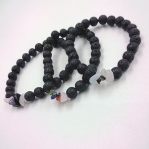 May include: Three black lava stone bracelets with gemstone accents. The bracelets are made of round, dark beads and feature small, polished stones in various colours, including pink, blue, and green.