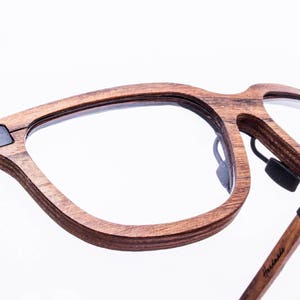May include: A pair of brown wood-framed eyeglasses with black arms. The glasses have a clear lens and a unique design.