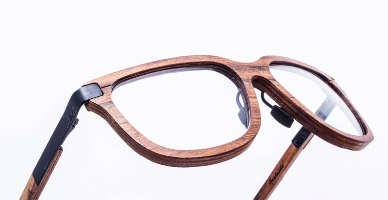 May include: A pair of brown wood-framed eyeglasses with black arms. The glasses have a clear lens and a unique design.