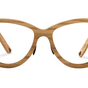 May include: A pair of cat-eye glasses with a wooden frame and clear lenses. The frame is a light brown color with a gold accent on the temples.