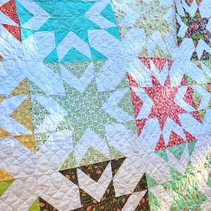 Könnte beinhalten: Eine Steppdecke mit weißem Hintergrund und einem Patchwork-Muster aus verschiedenen farbigen Sternen. Die Sterne bestehen aus verschiedenen Stoffen mit floralen und geometrischen Mustern. Die Steppdecke ist mit einem kreisförmigen Muster gesteppt.