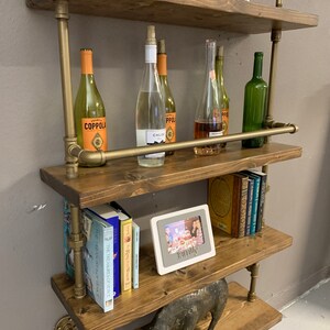 May include: A four-tiered industrial pipe shelf unit with wooden shelves. The shelves are decorated with books, wine bottles, a picture frame with the word "Family" on it, and decorative animal figurines.