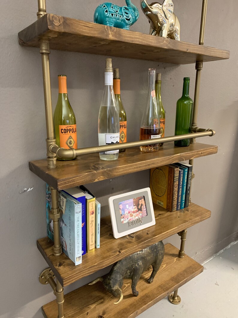 May include: A four-tiered industrial pipe shelf unit with wooden shelves. The shelves are decorated with books, wine bottles, a picture frame with the word "Family" on it, and decorative animal figurines.
