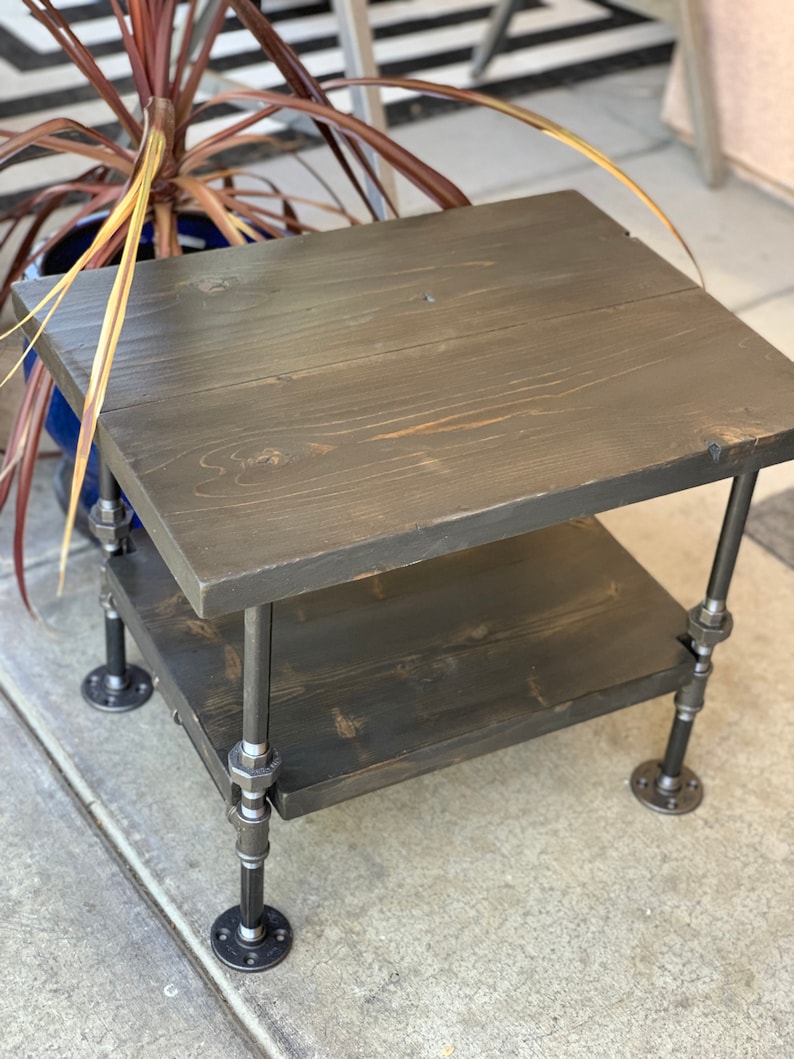 May include: A two-tiered wooden side table with black stained wood and black metal pipe legs.