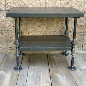 May include: A two-tiered industrial style table with black stained wooden shelves and black metal pipe legs.