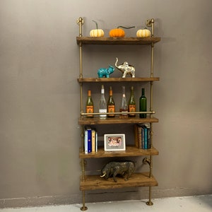 May include: A five-tiered industrial pipe shelf unit with wooden shelves. The shelves are decorated with pumpkins, elephants, wine bottles, books, a picture frame, and a bull figurine.