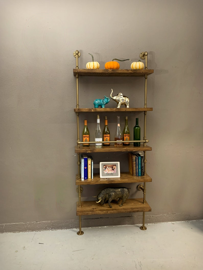 May include: A five-tiered industrial pipe shelf unit with wooden shelves. The shelves are decorated with pumpkins, elephants, wine bottles, books, a picture frame, and a bull figurine.