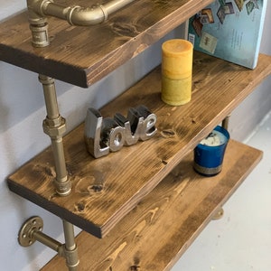 May include: Gold pipe shelving unit with wooden shelves. The shelves are decorated with candles, a book, and a silver 'love' sign.
