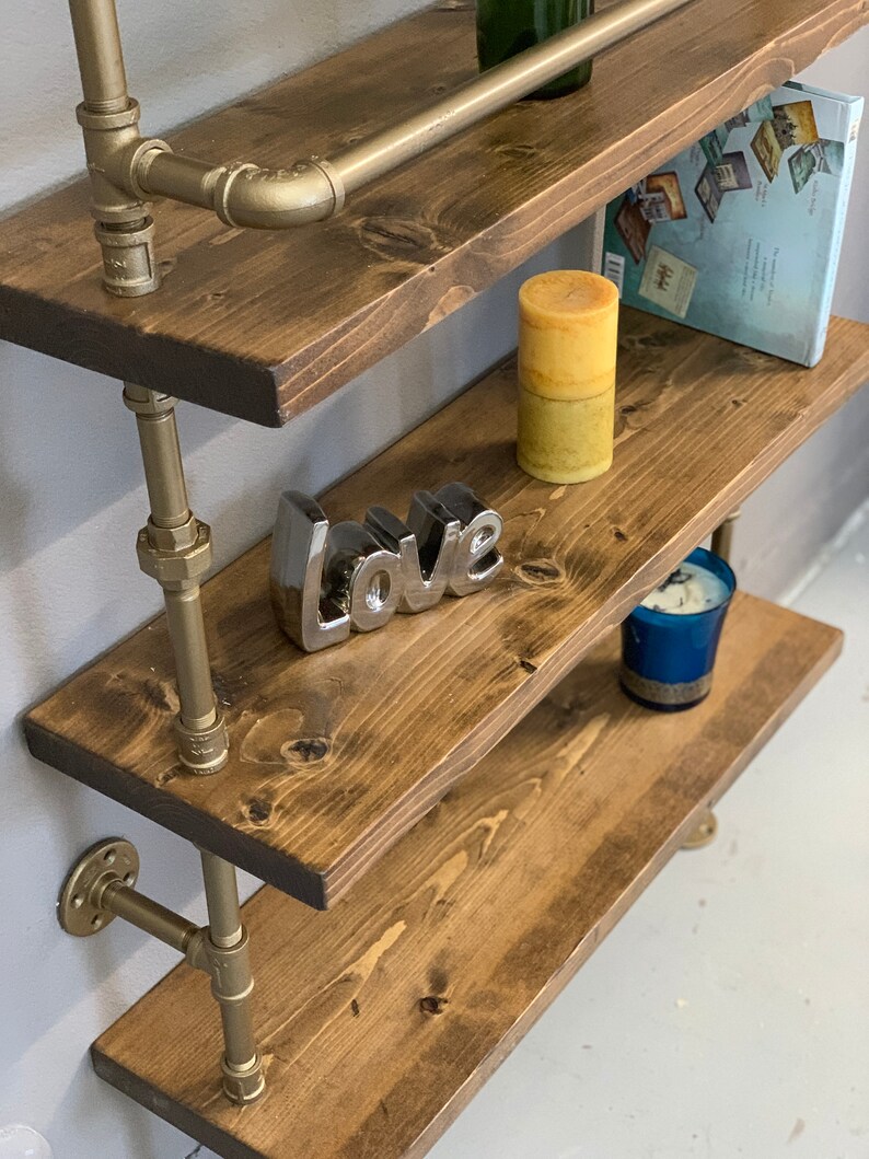 May include: Gold pipe shelving unit with wooden shelves. The shelves are decorated with candles, a book, and a silver 'love' sign.
