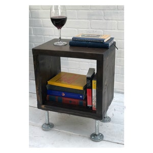 May include: A dark brown wooden end table with a square top and open shelf. The table has four silver metal legs and is decorated with a stack of books and a glass of red wine.