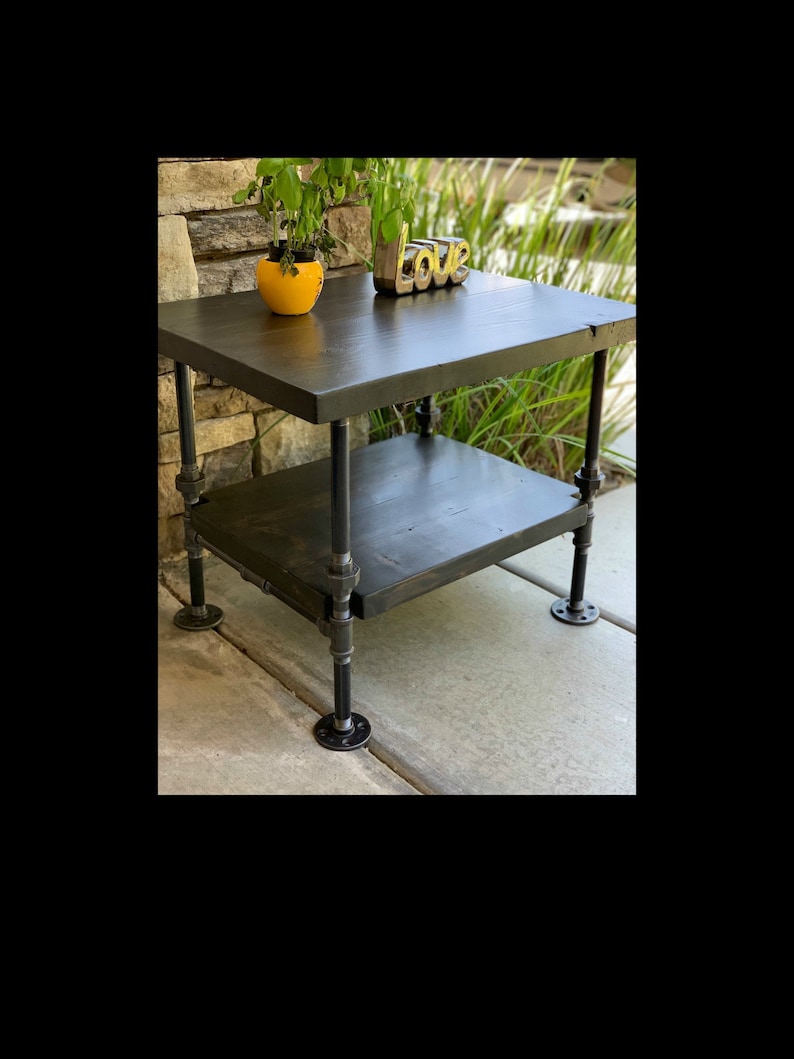 May include: A black two-tiered side table with a black metal frame and a wooden top. The table is decorated with a yellow potted plant and a gold "Love" sign.