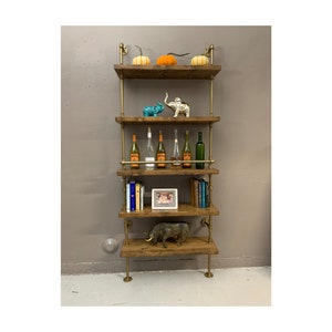 May include: A five-tiered industrial pipe shelf unit with wooden shelves. The shelves are decorated with pumpkins, elephants, wine bottles, books, a framed photo, and a small pig figurine.