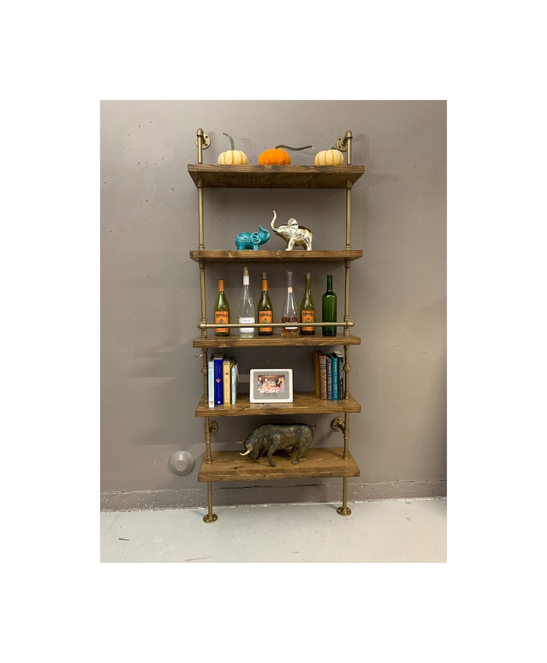 May include: A five-tiered industrial pipe shelf unit with wooden shelves. The shelves are decorated with pumpkins, elephants, wine bottles, books, a framed photo, and a small pig figurine.