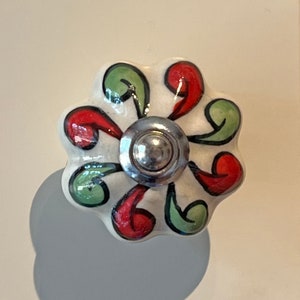 May include: White ceramic cabinet knob with a floral design in red, green, and black. The knob has a silver metal base.