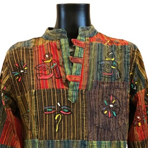 May include: A multi-coloured striped shirt with a mandarin collar and long sleeves. The shirt has a patchwork design with different coloured stripes and embroidered symbols. The shirt has a button closure at the neck.