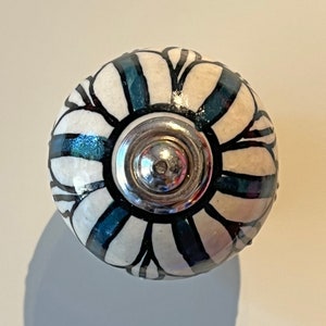 May include: White ceramic knob with a black and teal floral design and a silver metal centre.