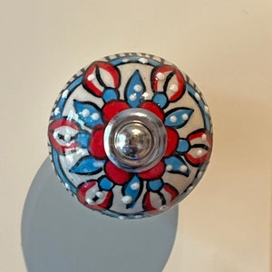 May include: A white ceramic knob with a blue and red floral design. The knob has a silver metal centre.