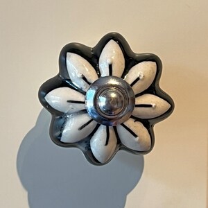 May include: Black and white ceramic flower-shaped cabinet knob with a silver centre.