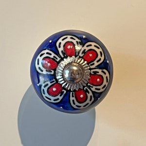 May include: A blue ceramic knob with a white and red floral design. The knob has a silver metal centre.