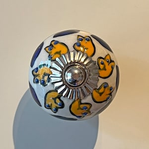 May include: White ceramic knob with a silver metal base. The knob is decorated with yellow and blue floral designs.