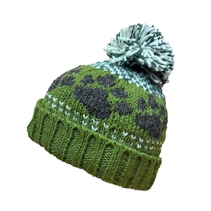May include: Green knitted hat with a white and grey patterned design and a white pom-pom on top.