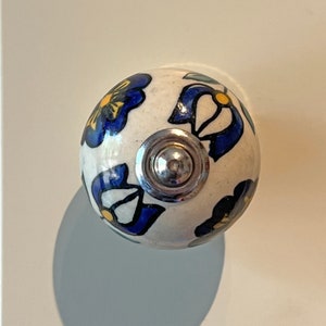 May include: White ceramic knob with a blue and yellow floral design. The knob has a silver metal base.
