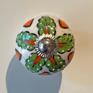 May include: White ceramic knob with a green and orange floral design and a silver metal centre.