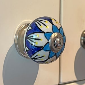 May include: A blue and white ceramic cabinet knob with a floral design. The knob has a silver metal base.