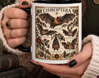 May include: A white ceramic mug with a black interior and handle, featuring a detailed botanical and zoological illustration of various bat species labeled CHIROPTERA, surrounded by intricate floral patterns and small text descriptions.