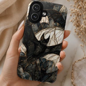 May include: A rectangular smartphone case featuring a dark, marble-like background with a repeating pattern of black bats with white, translucent wings. The design includes thin, gold-colored lines that outline the wings and create a geometric effect.