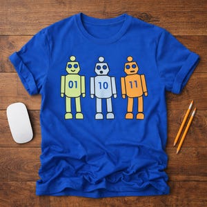 May include: Royal blue t-shirt featuring three cartoon robots in yellow, white, and orange. Each robot has a number: 01, 10, and 11. The shirt is on a wooden surface with a white computer mouse and two pencils.