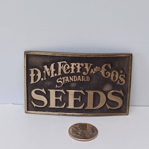 May include: A gold-colored metal belt buckle with the text "D.M. Ferry and Co's Standard Seeds" embossed on a black background.