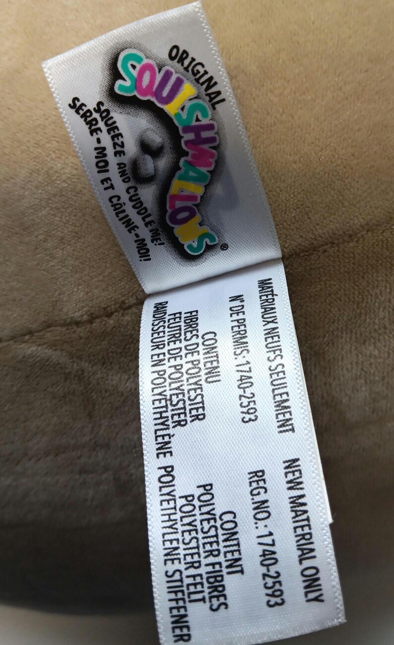 May include: A tag from a Squishmallows plush toy, featuring the brand name in colorful lettering. The tag includes the phrases "Squeeze and Cuddle Me!" and "New Material Only."