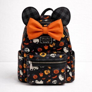 Op de afbeelding: Een zwarte mini-rugzak met een Halloween-patroon van geesten, schedels en oranje pompoenen. De tas heeft twee zwart-grijs geruite muizenoortjes aan de bovenkant, een grote oranje strik en een voorvak met ritssluiting en een Disney Parks Loungefly-label.