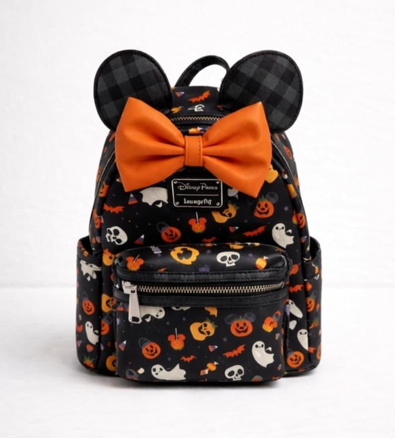 Op de afbeelding: Een zwarte mini-rugzak met een Halloween-patroon van geesten, schedels en oranje pompoenen. De tas heeft twee zwart-grijs geruite muizenoortjes aan de bovenkant, een grote oranje strik en een voorvak met ritssluiting en een Disney Parks Loungefly-label.