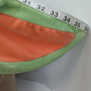 May include: A plush, green and orange costume ear with a measuring tape draped over it. The tape reads from 30 to 36 inches. The ear is green around the edges and orange in the center.