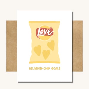 May include: A white card with a yellow bag of chips that says "Love" on it. The bag has three heart-shaped chips inside. The text at the bottom of the card says "Relation-Chip Goals".