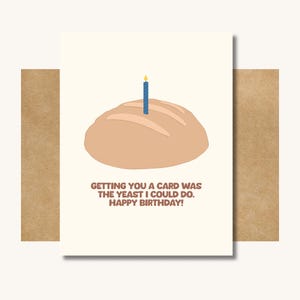 May include: A birthday card with a light brown loaf of bread with a blue candle on top. The card reads "Getting you a card was the yeast I could do. Happy Birthday!" The card is on a brown envelope.