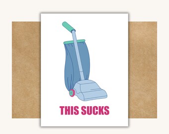 May include: A greeting card with a cartoon illustration of a vintage vacuum cleaner in shades of blue and green. The text "THIS SUCKS" is printed in pink below the vacuum. The card is set against a brown background.